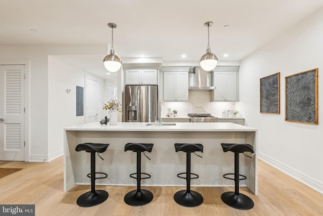 kitchen with stainless steel appliances, wall chimney exhaust hood, a kitchen island with sink, and decorative light fixtures