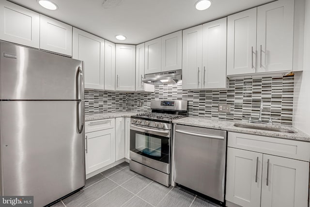 kitchen with light tile patterned floors, exhaust hood, backsplash, white cabinetry, and appliances with stainless steel finishes