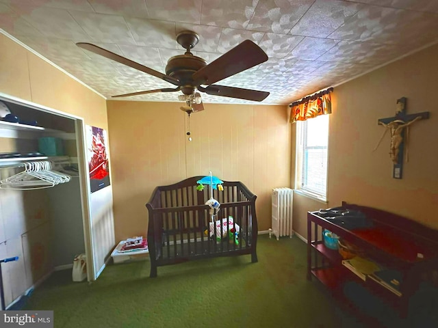 carpeted bedroom with a crib, ceiling fan, and radiator