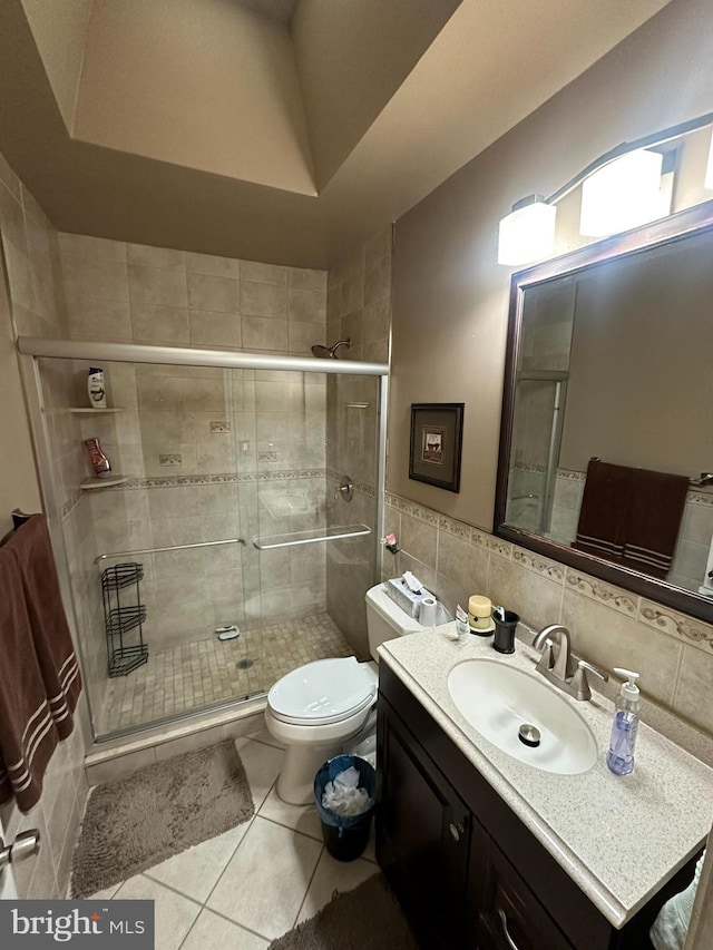 bathroom with tasteful backsplash, tile patterned floors, a shower with door, vanity, and toilet