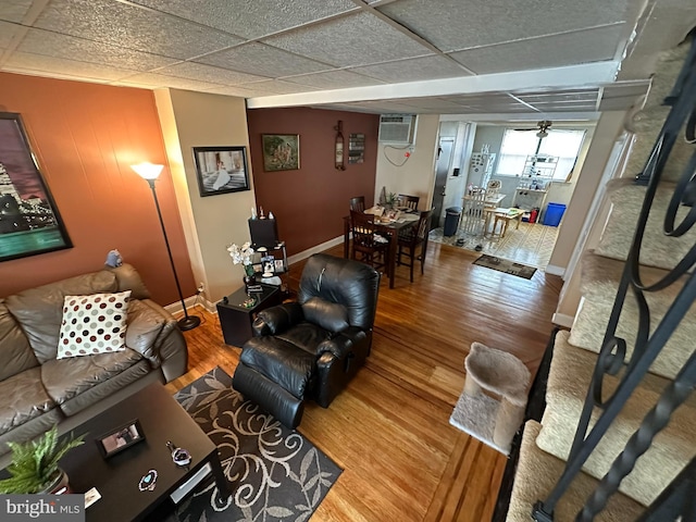 living room featuring hardwood / wood-style flooring, ceiling fan, an AC wall unit, and a drop ceiling