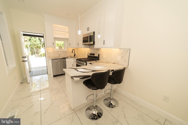 kitchen featuring kitchen peninsula, a kitchen breakfast bar, backsplash, white cabinetry, and appliances with stainless steel finishes