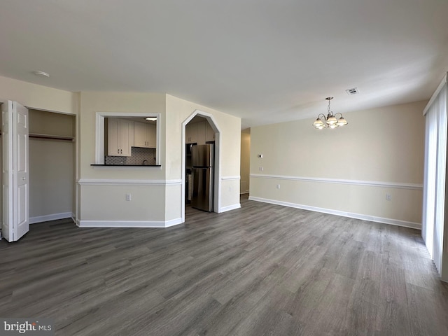 unfurnished living room with a chandelier, dark wood finished floors, and baseboards