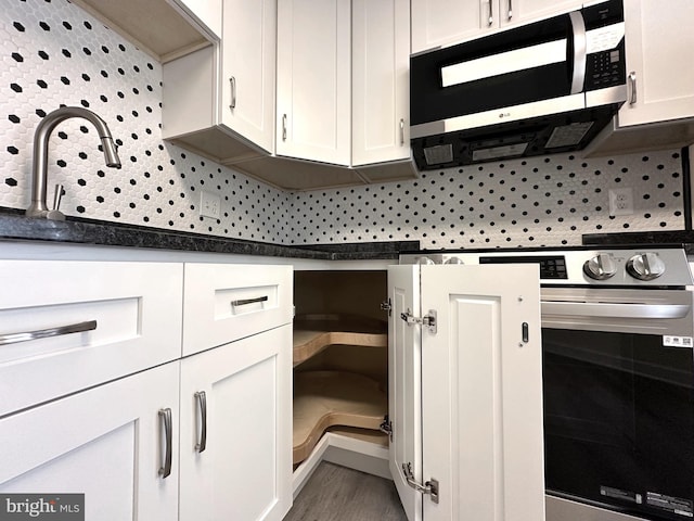 kitchen with backsplash, stove, white cabinets, and hardwood / wood-style flooring