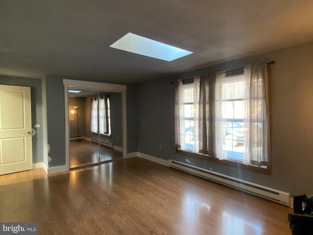 spare room with a skylight, a wealth of natural light, hardwood / wood-style floors, and a baseboard heating unit