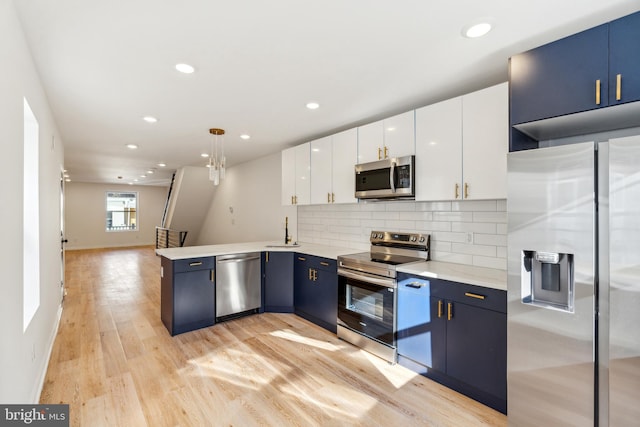 kitchen featuring stainless steel appliances, light wood-type flooring, hanging light fixtures, sink, and white cabinets