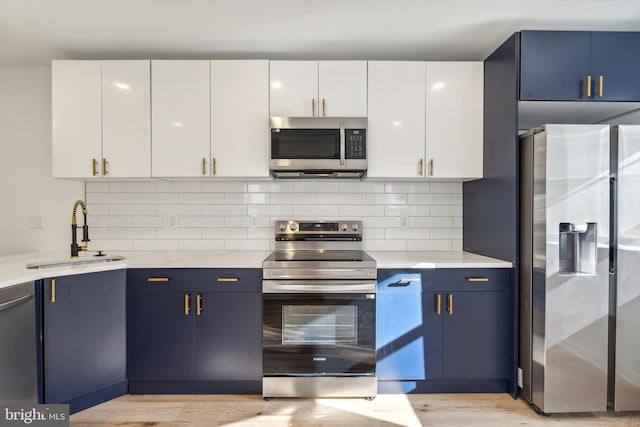 kitchen with white cabinets, blue cabinetry, sink, and appliances with stainless steel finishes