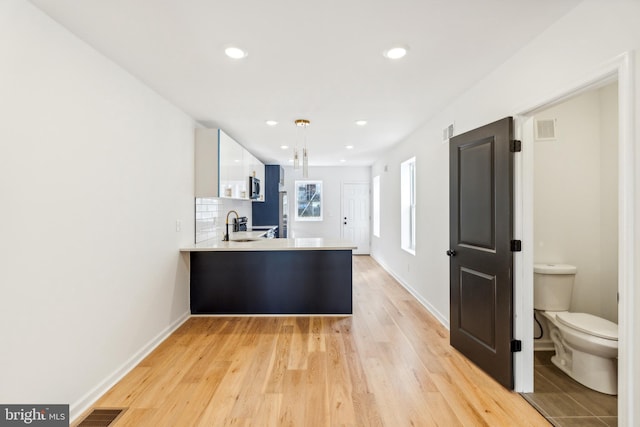 kitchen with kitchen peninsula, sink, tasteful backsplash, white cabinetry, and light hardwood / wood-style flooring