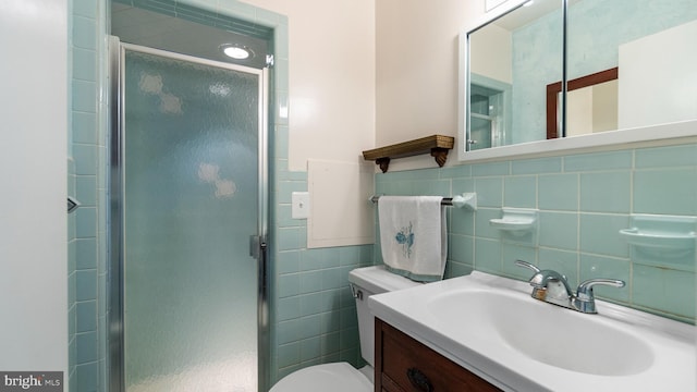 bathroom featuring a shower with door, vanity, toilet, and tile walls