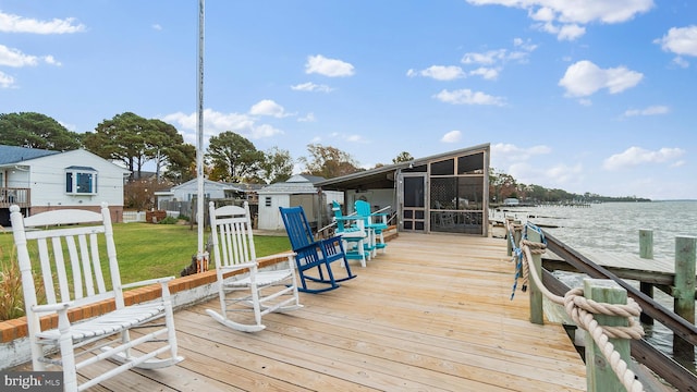 deck featuring a storage shed, a water view, a lawn, and a sunroom