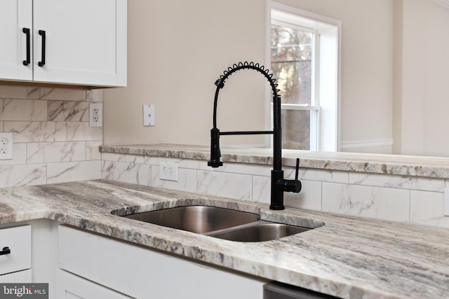 kitchen featuring decorative backsplash, white cabinetry, sink, and light stone counters