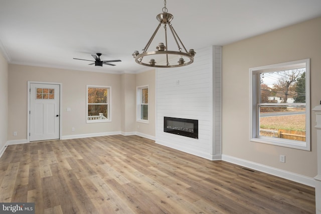 unfurnished living room featuring ceiling fan with notable chandelier, a large fireplace, hardwood / wood-style flooring, and crown molding