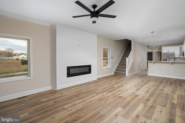 unfurnished living room featuring a large fireplace, ceiling fan, and light wood-type flooring