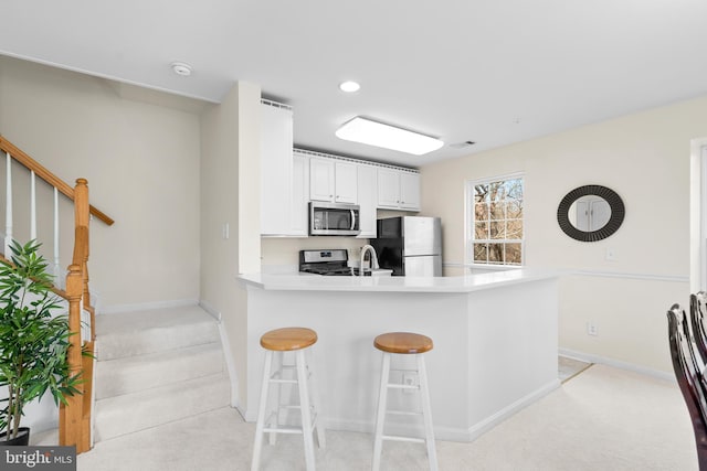 kitchen featuring kitchen peninsula, appliances with stainless steel finishes, light carpet, white cabinets, and a breakfast bar area