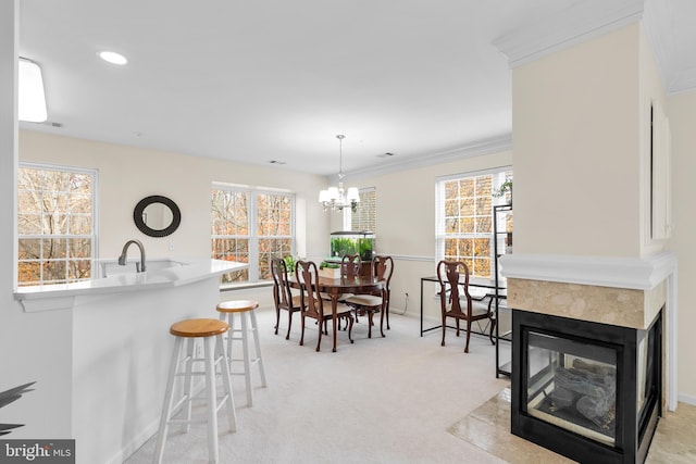 carpeted dining area with a multi sided fireplace, a chandelier, and ornamental molding