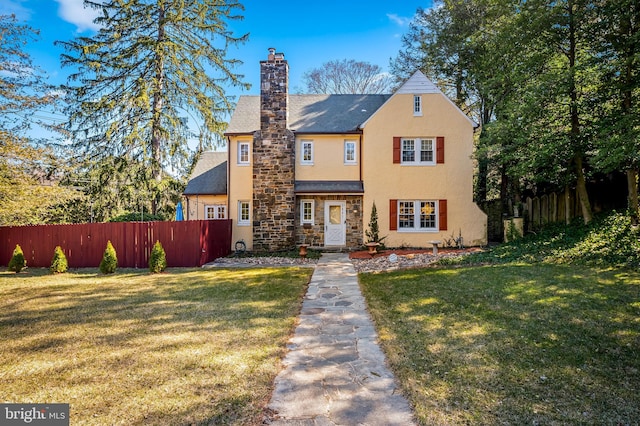 view of front facade with stucco siding, a front lawn, stone siding, fence, and a chimney