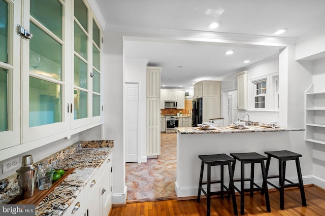 kitchen with stainless steel appliances, light stone countertops, a kitchen bar, and crown molding