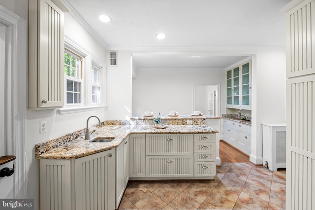 kitchen with visible vents, ornamental molding, a sink, light stone counters, and a peninsula