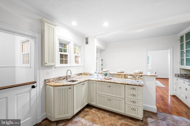 kitchen featuring light stone counters, visible vents, a peninsula, and a sink