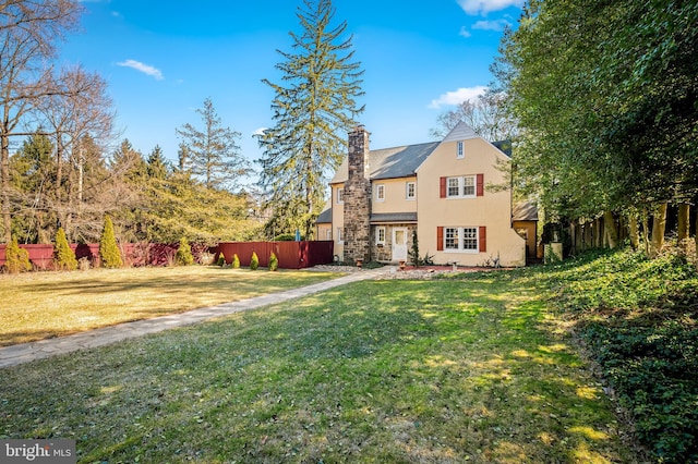 exterior space with a chimney, a lawn, fence, and stucco siding