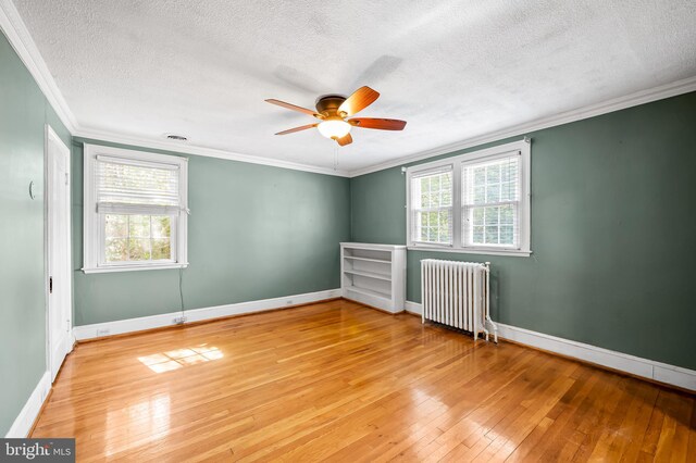 spare room featuring a textured ceiling, radiator, crown molding, light wood finished floors, and baseboards