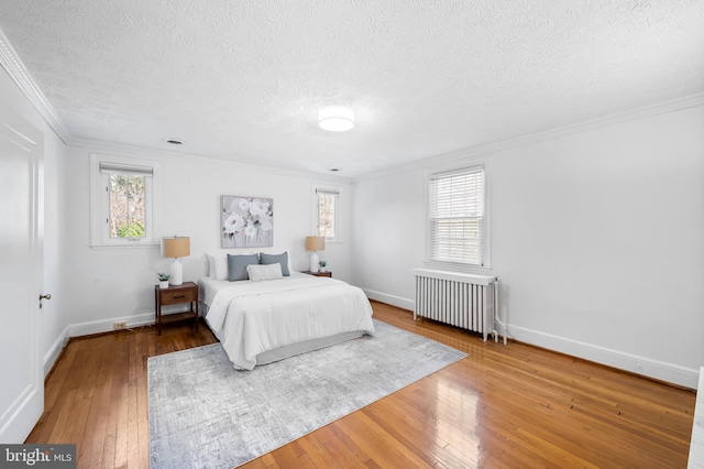 bedroom featuring hardwood / wood-style floors, radiator heating unit, baseboards, and ornamental molding