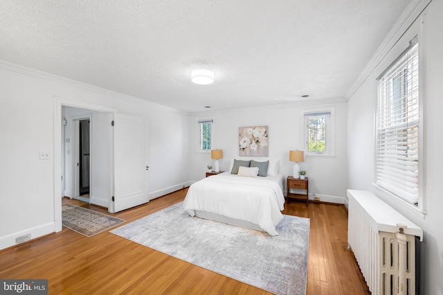 bedroom featuring crown molding, baseboards, light wood-type flooring, radiator heating unit, and a textured ceiling