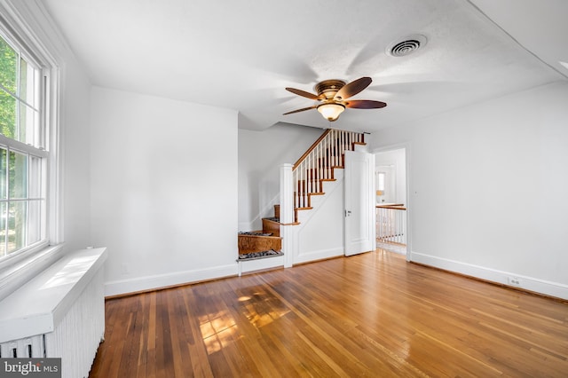 unfurnished living room featuring hardwood / wood-style flooring, radiator, a healthy amount of sunlight, and visible vents