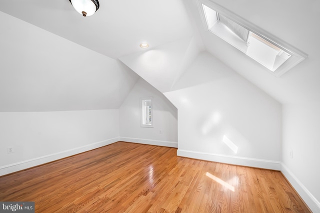 additional living space featuring baseboards, wood finished floors, and lofted ceiling with skylight