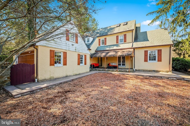 back of property with stucco siding, roof with shingles, and a patio area