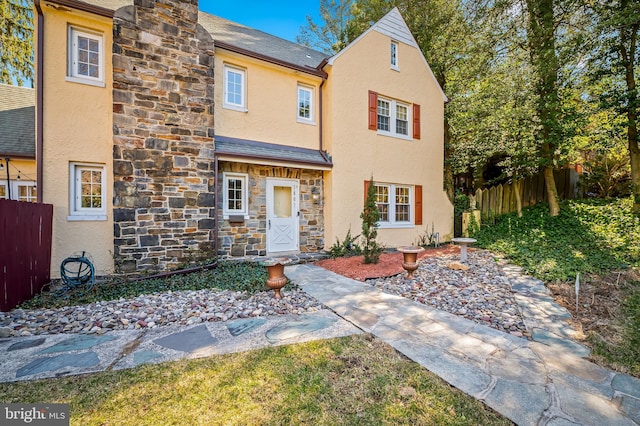 view of front of home with stucco siding, stone siding, and fence