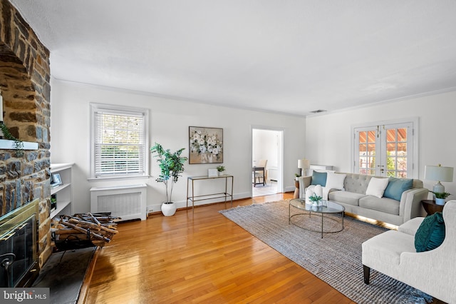 living room featuring hardwood / wood-style floors, a stone fireplace, radiator heating unit, and a healthy amount of sunlight