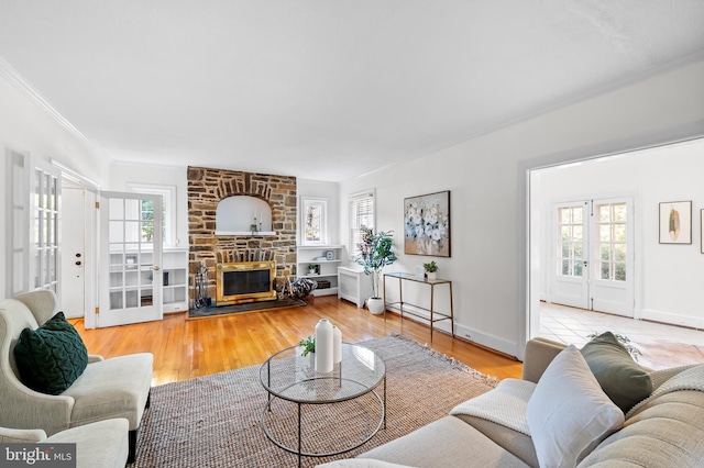 living area with baseboards, ornamental molding, a stone fireplace, french doors, and wood finished floors