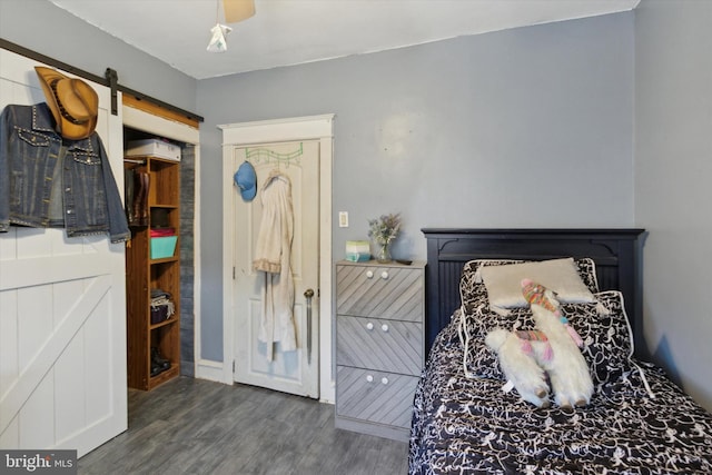 bedroom with a barn door, ceiling fan, and dark hardwood / wood-style flooring