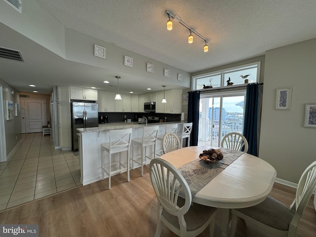 dining space with a textured ceiling, sink, light hardwood / wood-style flooring, and rail lighting