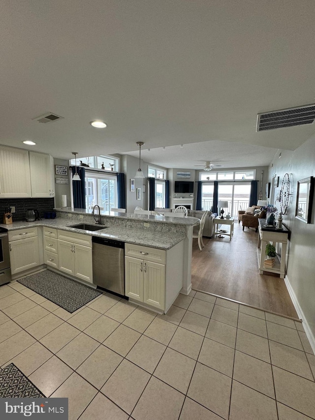 kitchen with sink, kitchen peninsula, appliances with stainless steel finishes, hanging light fixtures, and light hardwood / wood-style flooring