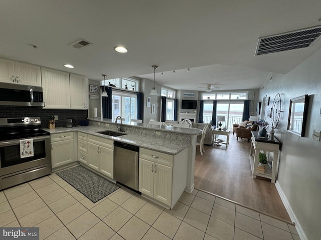 kitchen featuring light hardwood / wood-style floors, sink, kitchen peninsula, appliances with stainless steel finishes, and decorative light fixtures