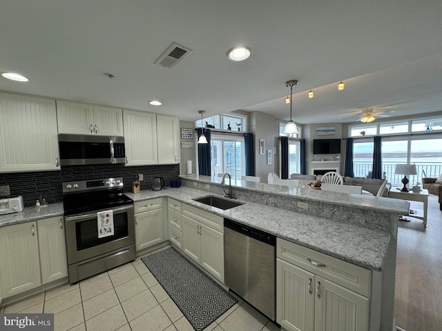 kitchen with appliances with stainless steel finishes, decorative light fixtures, decorative backsplash, sink, and kitchen peninsula