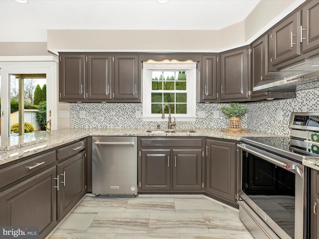 kitchen with dark brown cabinetry, sink, stainless steel appliances, tasteful backsplash, and light stone counters