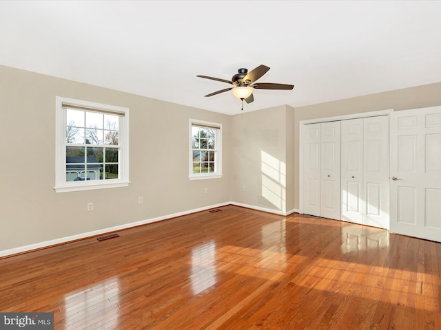 unfurnished bedroom with wood-type flooring, a closet, multiple windows, and ceiling fan