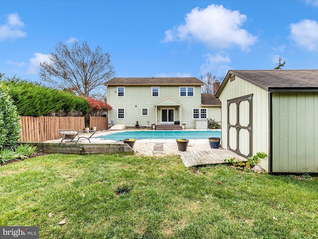 rear view of property with a yard, a covered pool, and a storage shed