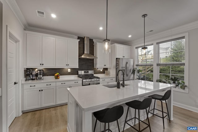 kitchen featuring stainless steel appliances, a center island with sink, sink, wall chimney exhaust hood, and decorative light fixtures