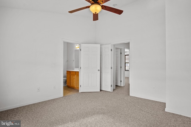 unfurnished bedroom featuring connected bathroom, light carpet, ceiling fan, and a high ceiling