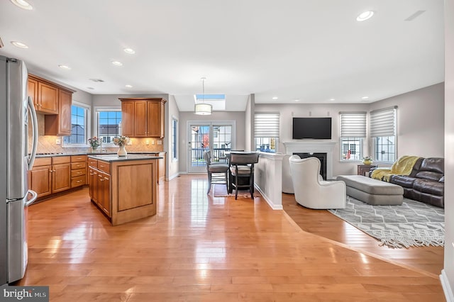 kitchen featuring light wood-type flooring, hanging light fixtures, decorative backsplash, and stainless steel refrigerator