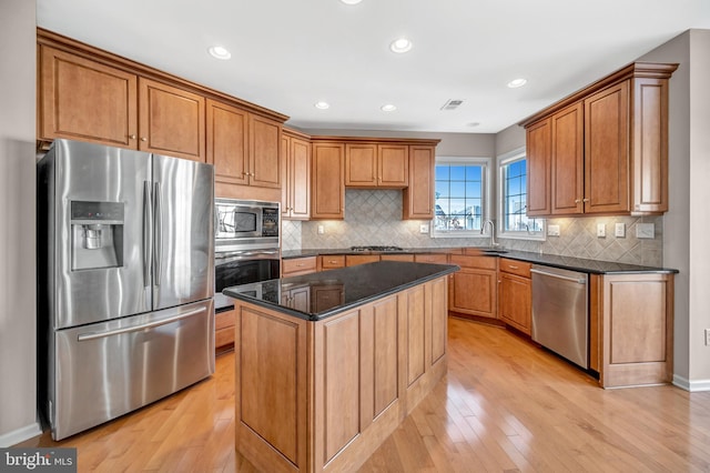 kitchen featuring appliances with stainless steel finishes, dark stone counters, a center island, light wood-type flooring, and decorative backsplash