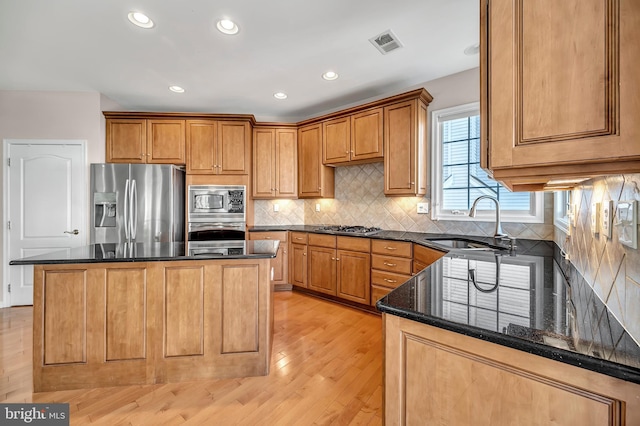 kitchen with stainless steel appliances, dark stone counters, a kitchen island, sink, and light hardwood / wood-style floors