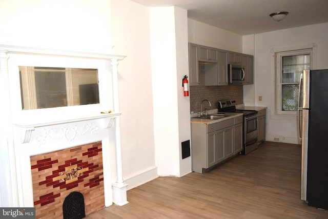 kitchen featuring gray cabinetry, sink, stainless steel appliances, light hardwood / wood-style floors, and decorative backsplash