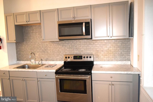 kitchen with decorative backsplash, gray cabinets, sink, and appliances with stainless steel finishes