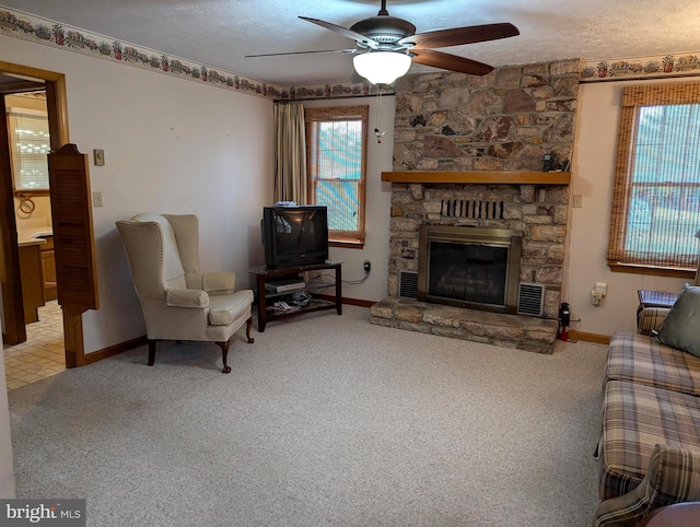 carpeted living room with a stone fireplace, a textured ceiling, and ceiling fan