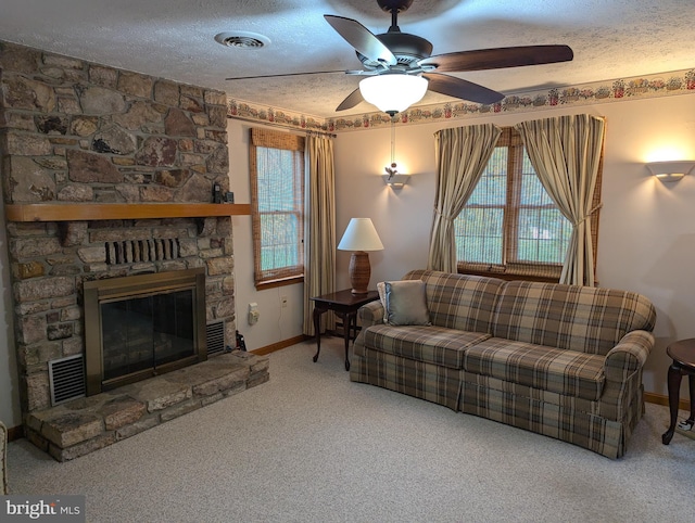 living room with a stone fireplace, a textured ceiling, carpet flooring, and ceiling fan